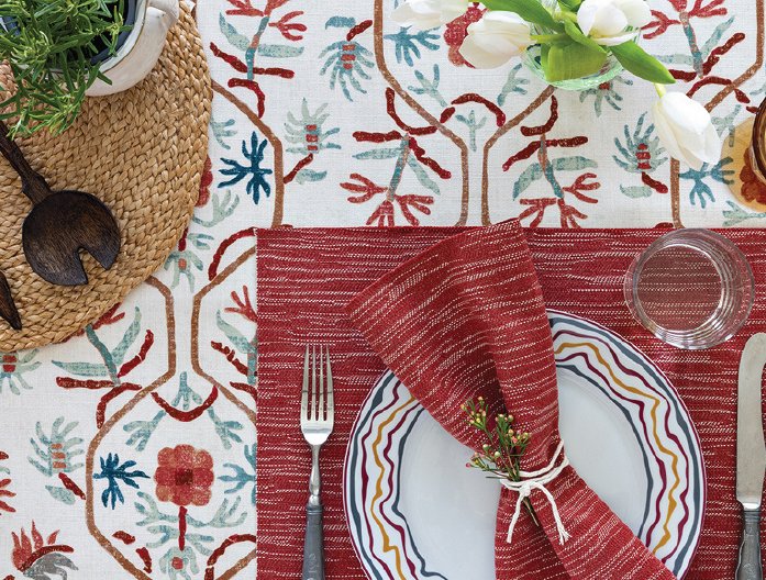 Table setting styled with red napkins and plates on floral fabric from the L'eternel Ete collection by GP & J Baker